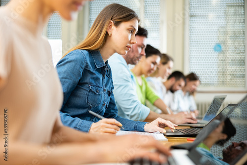 Group of students studying in the auditorium at study time, searches for information on a laptop and writes it out in a ..copybooks
