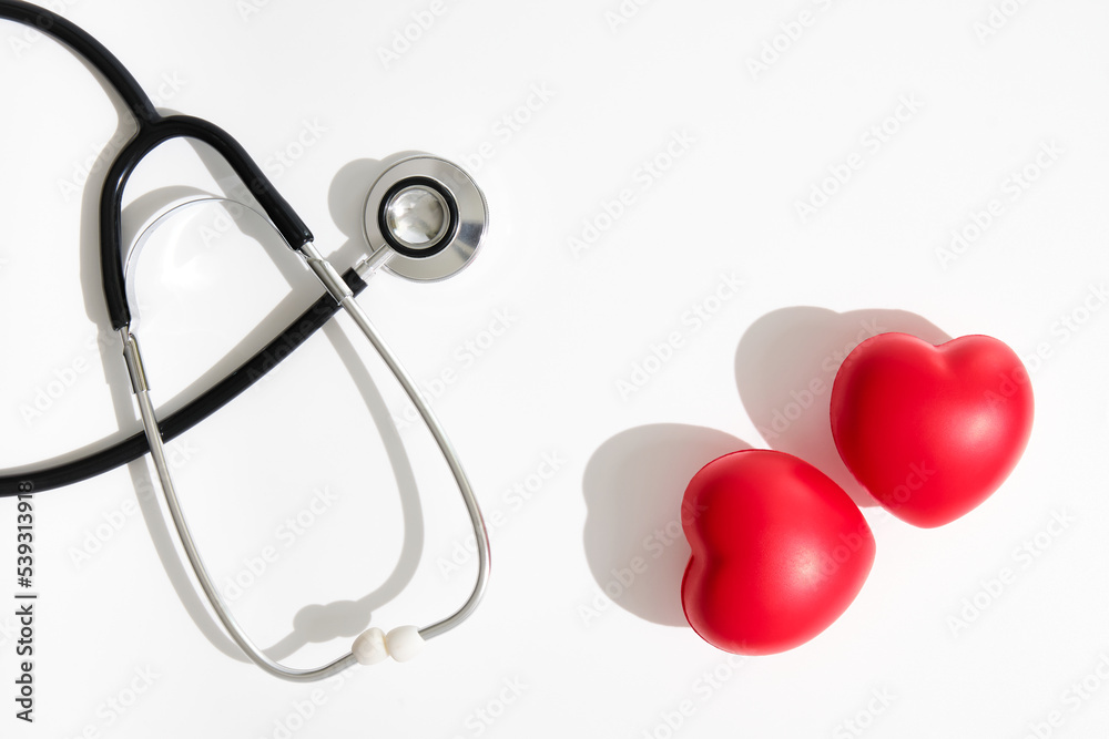 image from above of two red hearts and a black stethoscope on the other side of the image with hard shadows on a white background image from above of two red hearts and a black stethoscope on the other side of the image with hard shadows on a white background