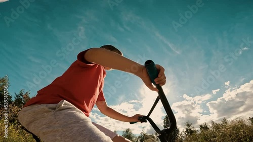 Overjoyed male kid fast riding bicycle surrounded by summer sunny clear blue sky natural forest park