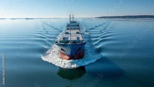 Aerial forward view of general cargo vessel making way ahead in Finnish archipelago during spring time. Glassy sea surface. photo