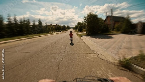 Father follow to boy kid speed riding on bike at asphalt road countryside nature sunny day POV shot