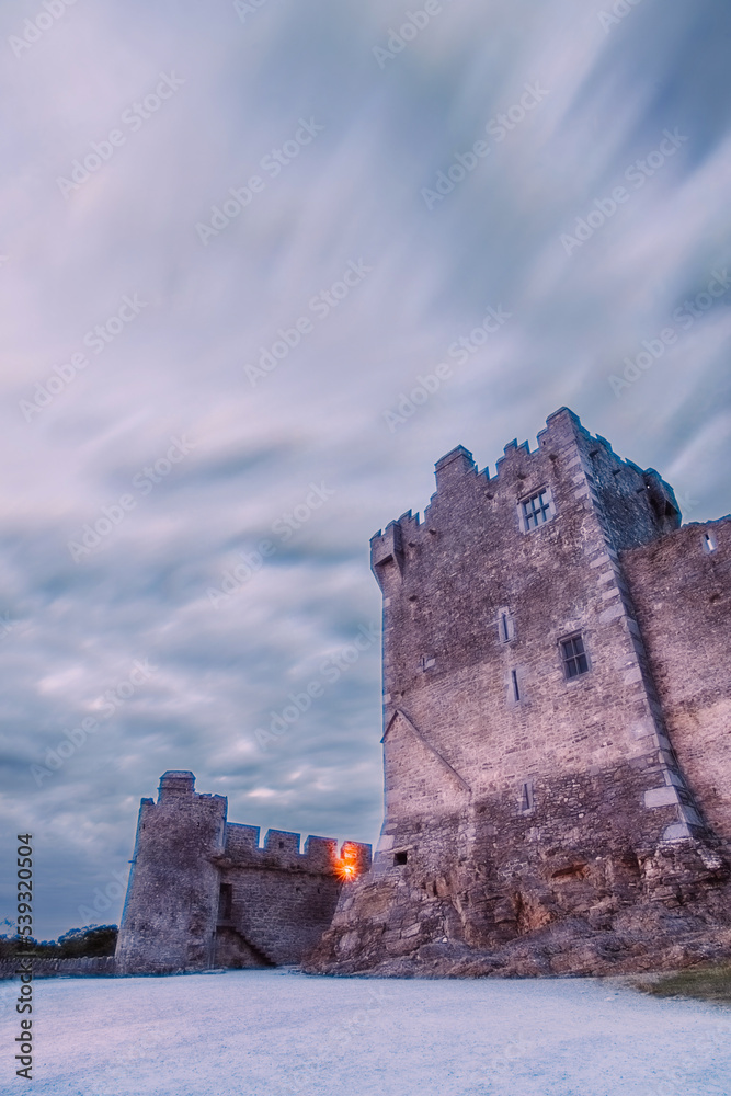 Fototapeta premium Ancient old Fortress Ross Castle ruin with a lake, green grass and orange clouds. Killarney national park, co Kerry, Ireland. High quality photo