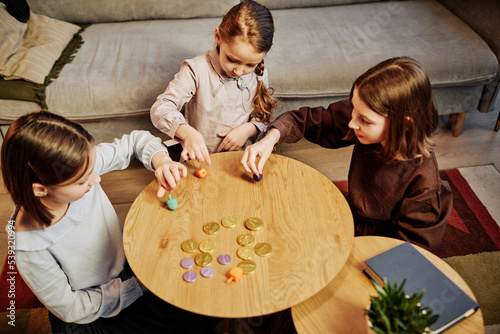 High angle portrait of three girls playing dreidel game in cozy home setting, copy space photo