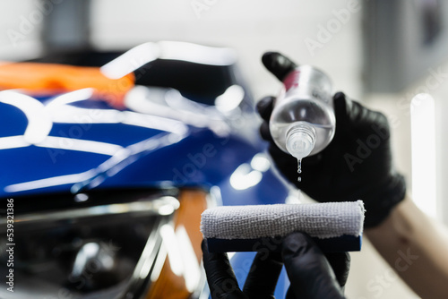 Detailing service worker applies ceramic protective liquid on sponge close-up. Process of pouring ceramic liquid from bottle on sponge to apply protective coating on car.