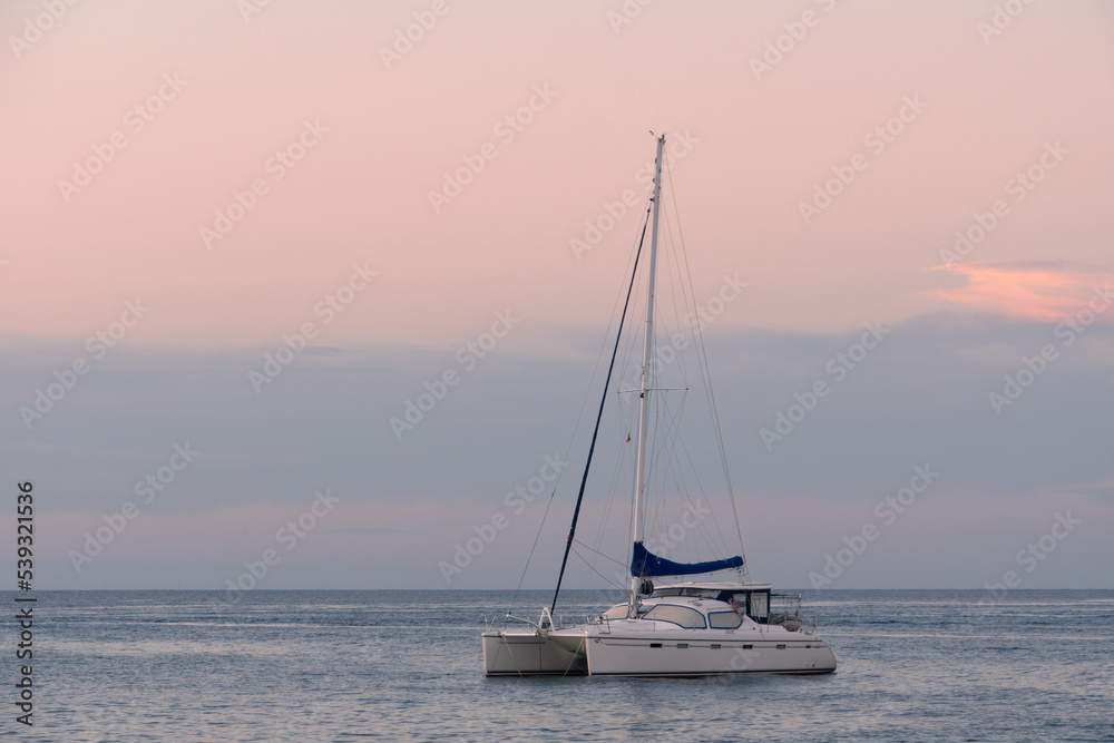Single-deck sailing yacht on the sea in calm. Lonely empty boat at sunset during the golden hour. A boat against a pink-blue sky.