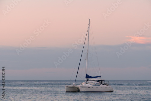 Single-deck sailing yacht on the sea in calm. Lonely empty boat at sunset during the golden hour. A boat against a pink-blue sky. © Semyon_Nazarov	