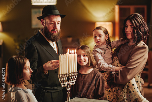 Fototapeta Portrait of happy jewish family lighting menorah candle during Hanukkah celebrat