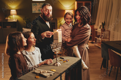 Canvas Print Portrait of modern jewish family lighting silver menorah candle during Hanukkah