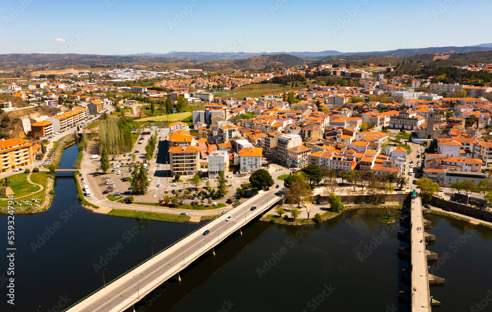 Scenic drone view of Mirandela, small Portuguese city on banks of Tua overlooking terracotta roofs of residential buildings and two bridges across river on sunny spring day