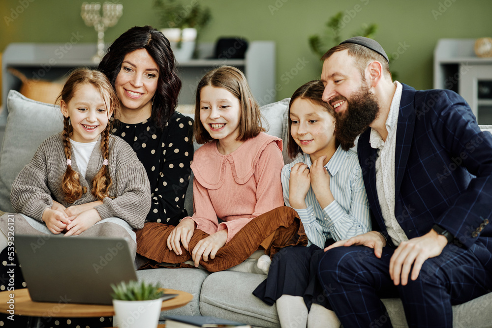 Portrait of modern jewish family using laptop and calling by video chat in cozy home setting Portrait of modern jewish family using laptop and calling by video chat in cozy home setting