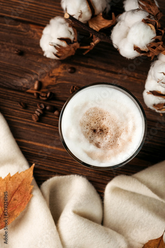 coffee latte with foam in a glass on a wooden table. next to a branch of cotton, dry leaves and a white plaid