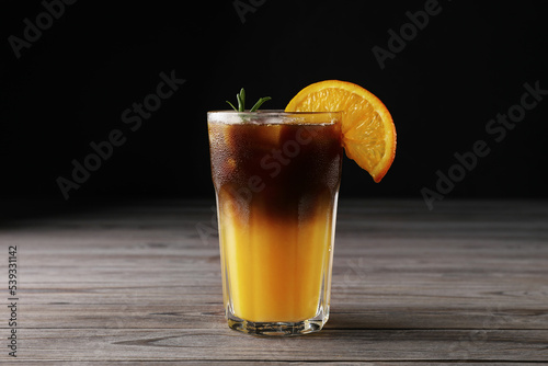 Tasty refreshing drink with coffee and orange juice on wooden table against dark background