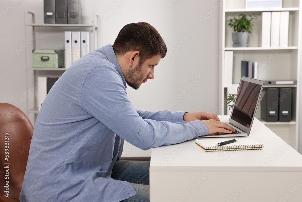 Man with poor posture working on laptop in office. Symptom of scoliosis - obrazy, fototapety, plakaty 