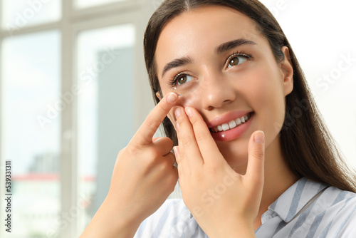 Woman putting contact lens in her eye at home