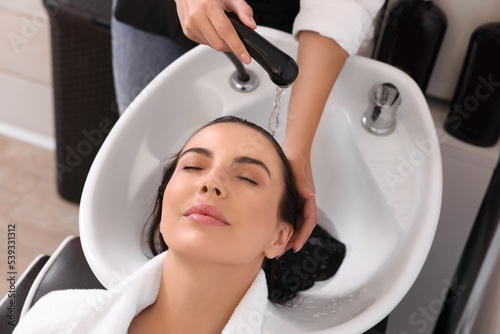 Professional hairdresser washing woman's hair in beauty salon, closeup