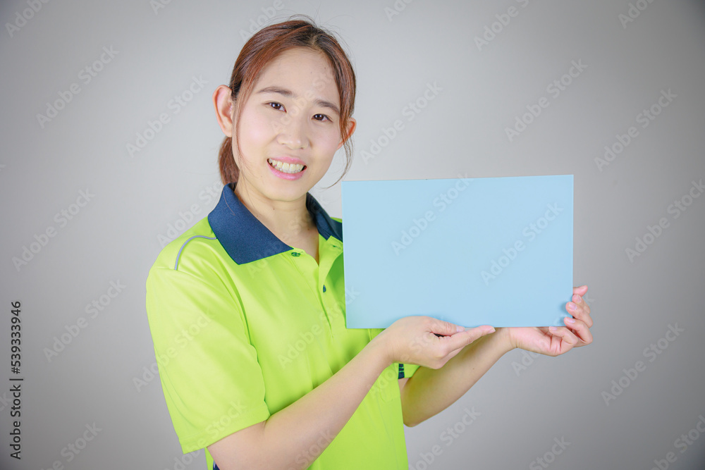 水色のメッセージボードを持つ作業服の日本人女性(左向き) 水色のメッセージボードを持つ作業服の日本人女性(左向き)