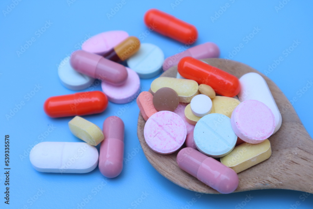 Capsules pill in wooden spoon on blue background. Antibiotics drug resistance. Antimicrobial capsule pills. Pharmaceutical industry. With space for text or image. Capsules pill in wooden spoon on blue background. Antibiotics drug resistance. Antimicrobial capsule pills. Pharmaceutical industry. With space for text or image.