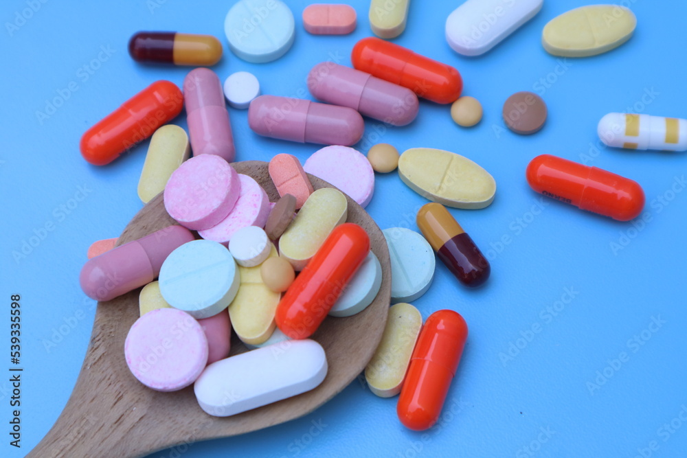 Capsules pill in wooden spoon on blue background. Antibiotics drug resistance. Antimicrobial capsule pills. Pharmaceutical industry. With space for text or image. Capsules pill in wooden spoon on blue background. Antibiotics drug resistance. Antimicrobial capsule pills. Pharmaceutical industry. With space for text or image.