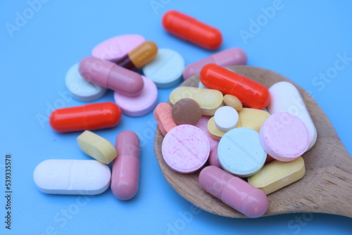 Capsules pill in wooden spoon on blue background. Antibiotics drug resistance. Antimicrobial capsule pills. Pharmaceutical industry. With space for text or image. 