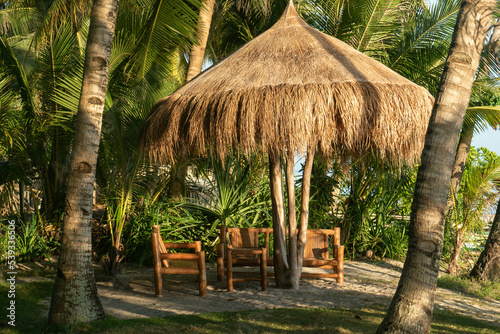 outdoor patio set made from all natural materials by local craftsman is set up in shore side beach front property of resort like hotel  with shade from dried plant material and palm fronds