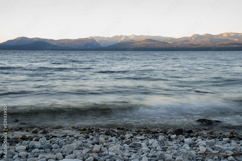 Long exposure shot of Nahuel Huapi lake at sunset. Beautiful blurred water effect, the rocky shore and dusk colors.