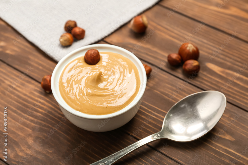 Bowl of tasty hazelnut butter on wooden background