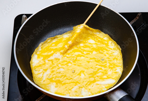 調理中の写真　薄焼き卵をフライパンで焼く　卵の表面が乾いたら、串で端を掬い上げる
