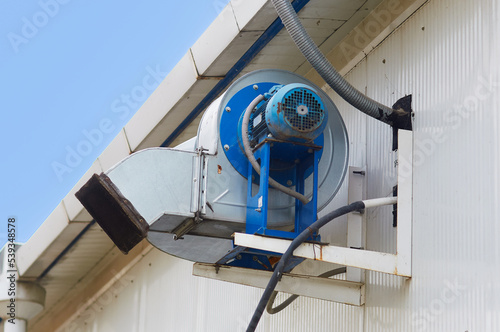 The air exhaust system is installed outside the building. Electrical equipment for extracting and filtering air. Blue electric motor with an air duct on the wall of the building. Selective focus
