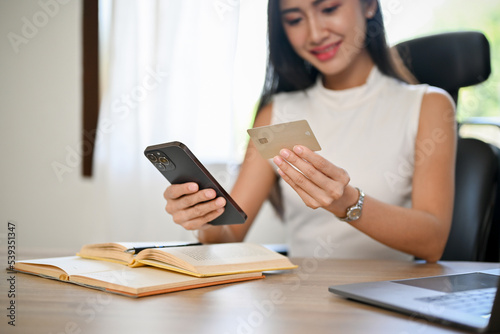 Attractive Asian businesswoman at her desk, holding a mobile phone and a credit card