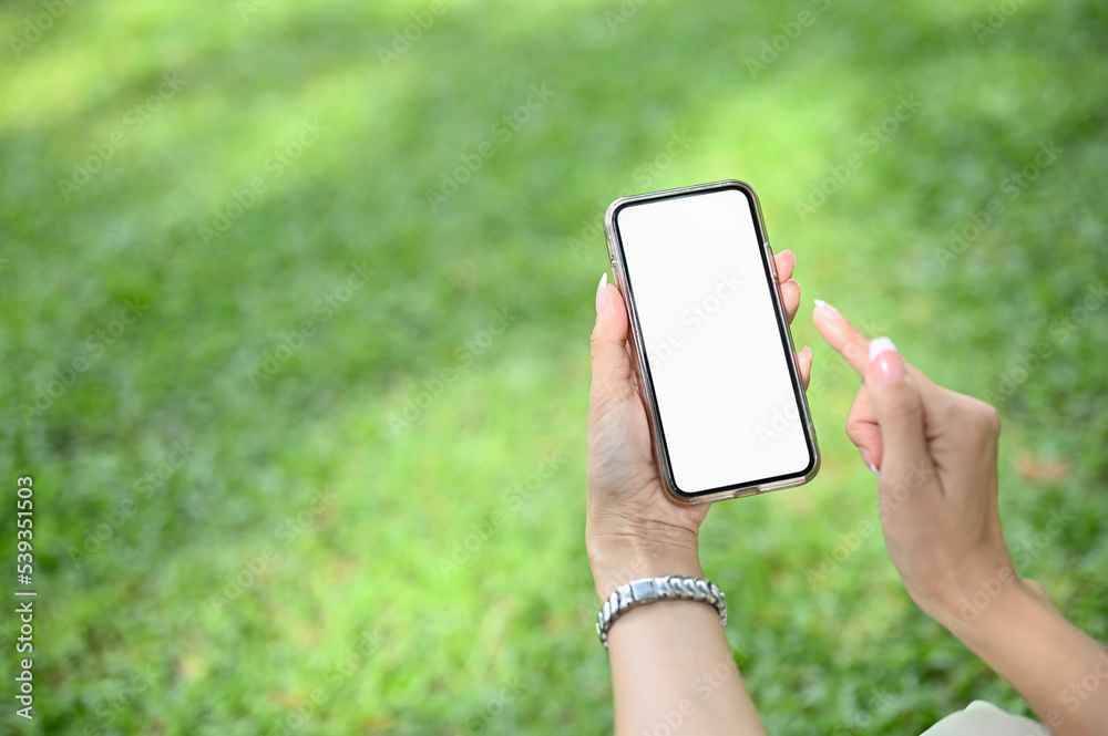 A smartphone mockup is in a woman's hand over blurred green grass background.