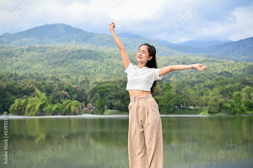 Carefree and relaxed Asian female breathing fresh air  standing over the beautiful mountain and lake