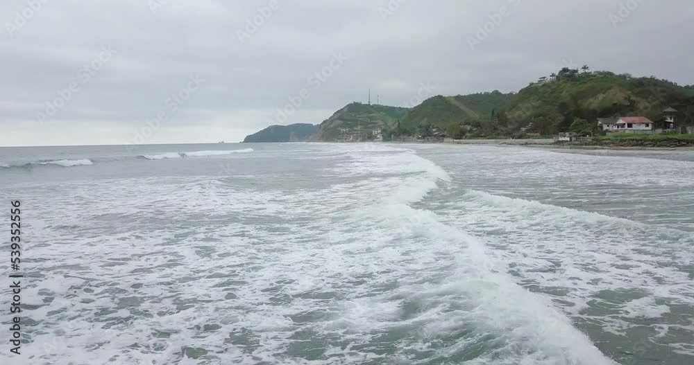 Aerial drone view of waves splashing at the shore of Olon beach in Ecuador. In the back of the scene is the ocean's horizon, some beach houses and the beach. Cloudy day. Aerial drone view of waves splashing at the shore of Olon beach in Ecuador. In the back of the scene is the ocean's horizon, some beach houses and the beach. Cloudy day.