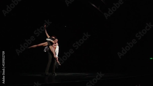 Latin-American ballroom dancers couple.Man brings woman on dark stage,picks her up,rotates her turning around his neck,puts her bented on shoulder,spinning around holding her leg in beautiful pose.