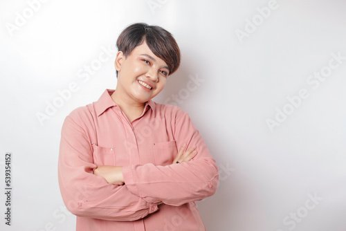 Portrait of a confident smiling Asian woman wearing pink shirt standing with arms folded and looking at the camera isolated over white background