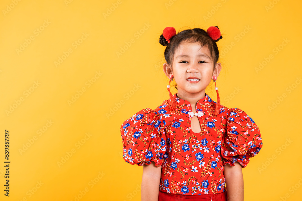 Happy Asian Chinese little girl smile wearing red cheongsam, Portrait children in traditional dress with greeting gesture celebration for Chinese New Year, studio short isolated on yellow background Happy Asian Chinese little girl smile wearing red cheongsam, Portrait children in traditional dress with greeting gesture celebration for Chinese New Year, studio short isolated on yellow background