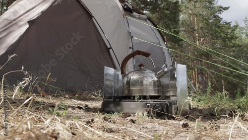 a kettle boils on a tourist gas stove in a camping near a tent