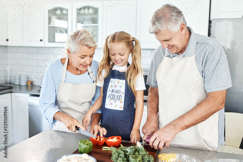 Grandparents, girl child in kitchen and cooking healthy food with vegetables on cutting board for happy family lunch at home. Natural, organic nutrition and clean diet for senior people in retirement