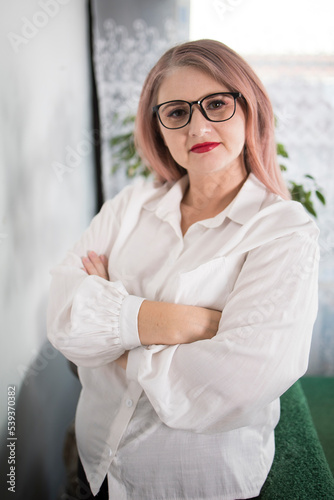 Portrait of an adult woman entrepreneur with grayish hair in a managerial position, dressed in a white blouse and busy working in the office