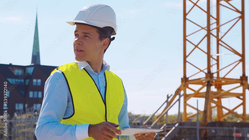 Professional builder standing in front of construction site. Foreman in hardhat helmet and vest. Office building and crane background. Business, real estate and investment. Professional builder standing in front of construction site. Foreman in hardhat helmet and vest. Office building and crane background. Business, real estate and investment.