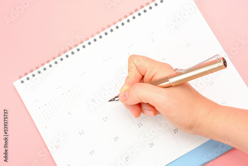 Female hands write in calendar on pink background, concept of planning.