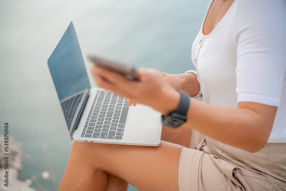 Naklejka premium Freelance close up woman hands writing on computer. Well looking middle aged woman typing on laptop keyboard outdoors with beautiful sea view.