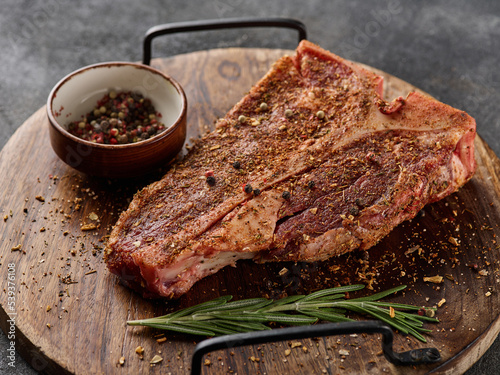Raw fresh meat T-bone steak, seasoning on chopping cutting wooden board on grey background.