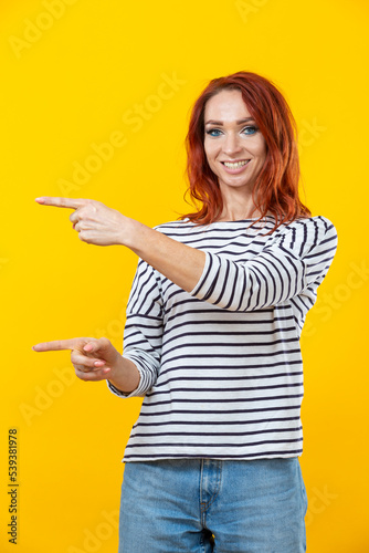 Happy excited cuacaisan winsome ginger girl in striped shirt pointing with two fingers isolated on golden yellow background