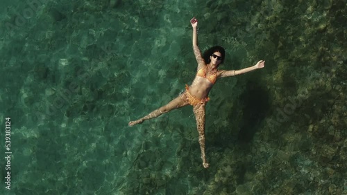Wallpaper Mural Aerial view of a beautiful woman wearing an orange bikini while floating and sunbathing in a transparent sea in San Sostene, Calabria, Italy. Torontodigital.ca