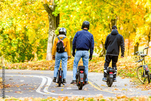 Three guys on a monowheel ride through the autumn park
