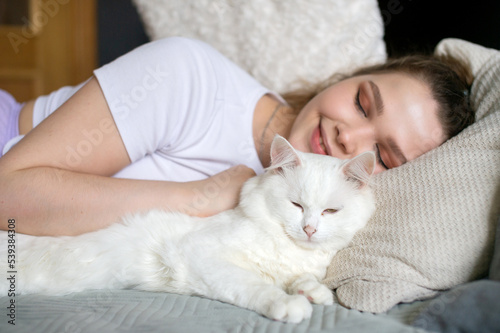 Cute girl sleeping on a bed next to a white cat