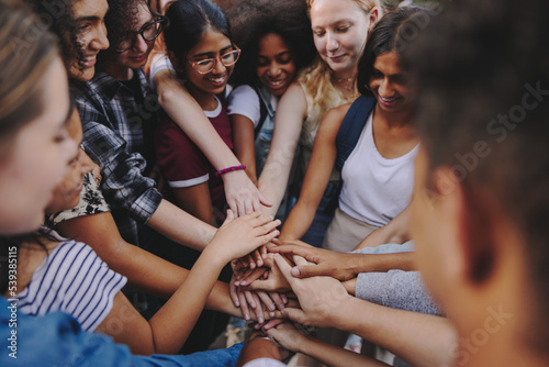 Diverse teenagers putting their hands together in unity photo