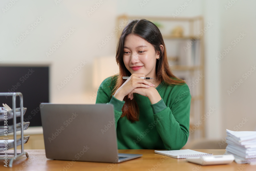 Bright, cute and happy Asian female student study online in the living room using laptop computer in a relaxed manner. Young Asian woman using laptop at home. Bright, cute and happy Asian female student study online in the living room using laptop computer in a relaxed manner. Young Asian woman using laptop at home.