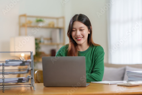 Bright, cute and happy Asian female student study online in the living room using laptop computer in a relaxed manner. Young Asian woman using laptop at home.