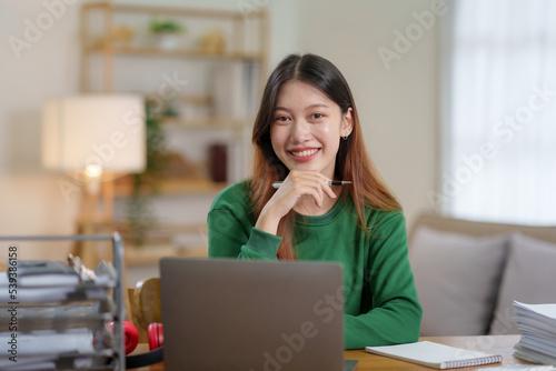 Bright, cute and happy Asian female student study online in the living room using laptop computer in a relaxed manner. Young Asian woman using laptop at home.